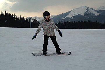 a girl in a patterned snowboard jacket learning to snowboard
