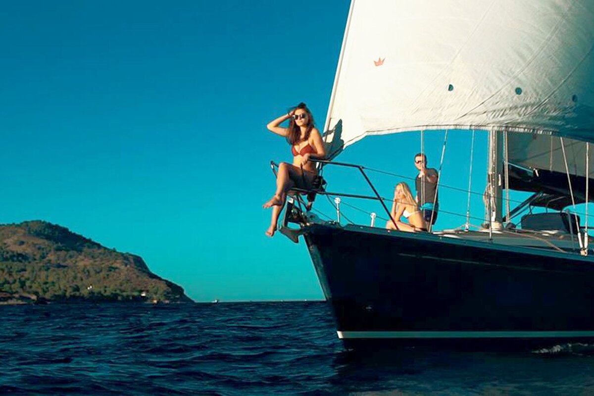 A woman in a bikini sits on the bow of a sailboat