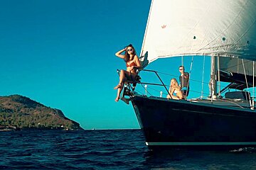 A woman in a bikini sits on the bow of a sailboat