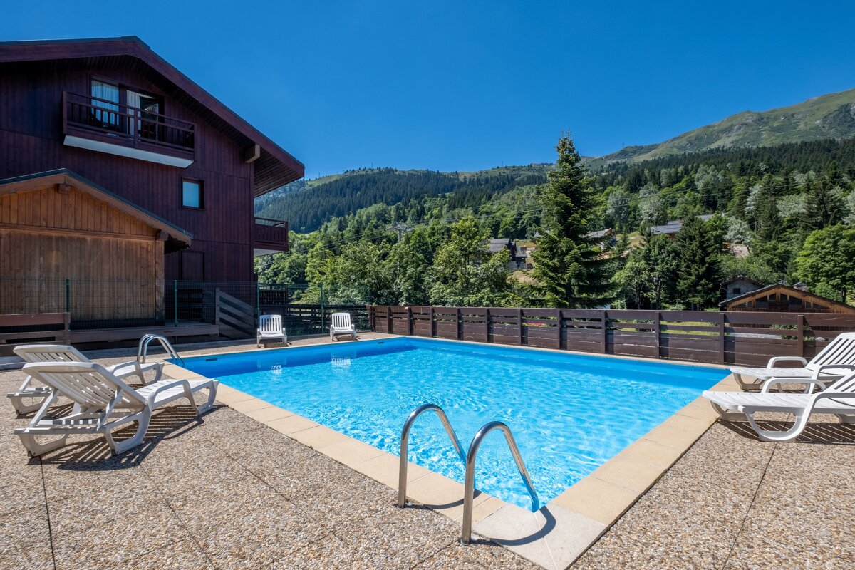 A large swimming pool surrounded by chairs and a fence with mountains in the background