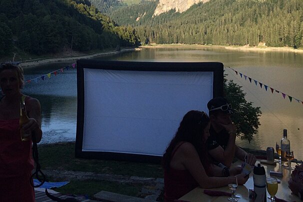 A group of people sitting around a table with a large screen in the background