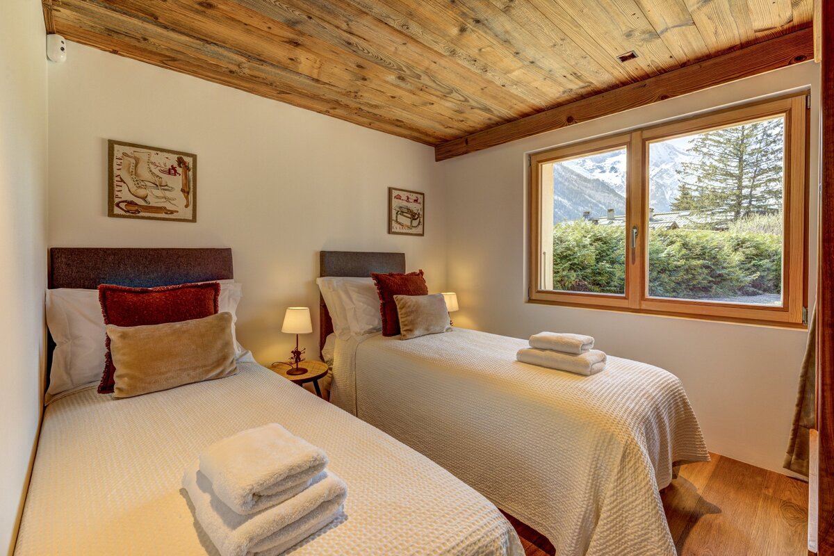 A bedroom with two twin beds and a window with mountains in the background
