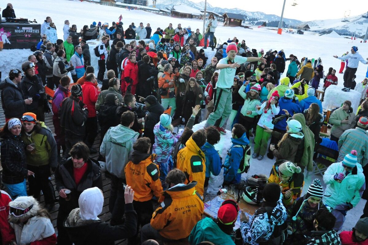 A group of people are gathered in a snowy area and one of them is wearing a jacket that says driftwood club