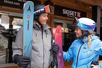 A man and a woman holding skis in front of a ski set store