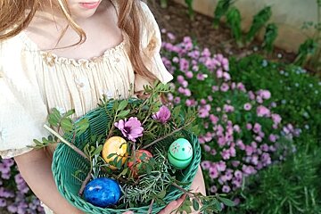 A girl is holding a basket of flowers and eggs
