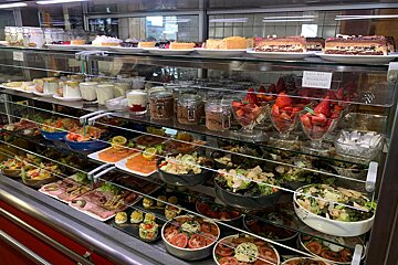 A display case filled with a variety of food including salads and desserts