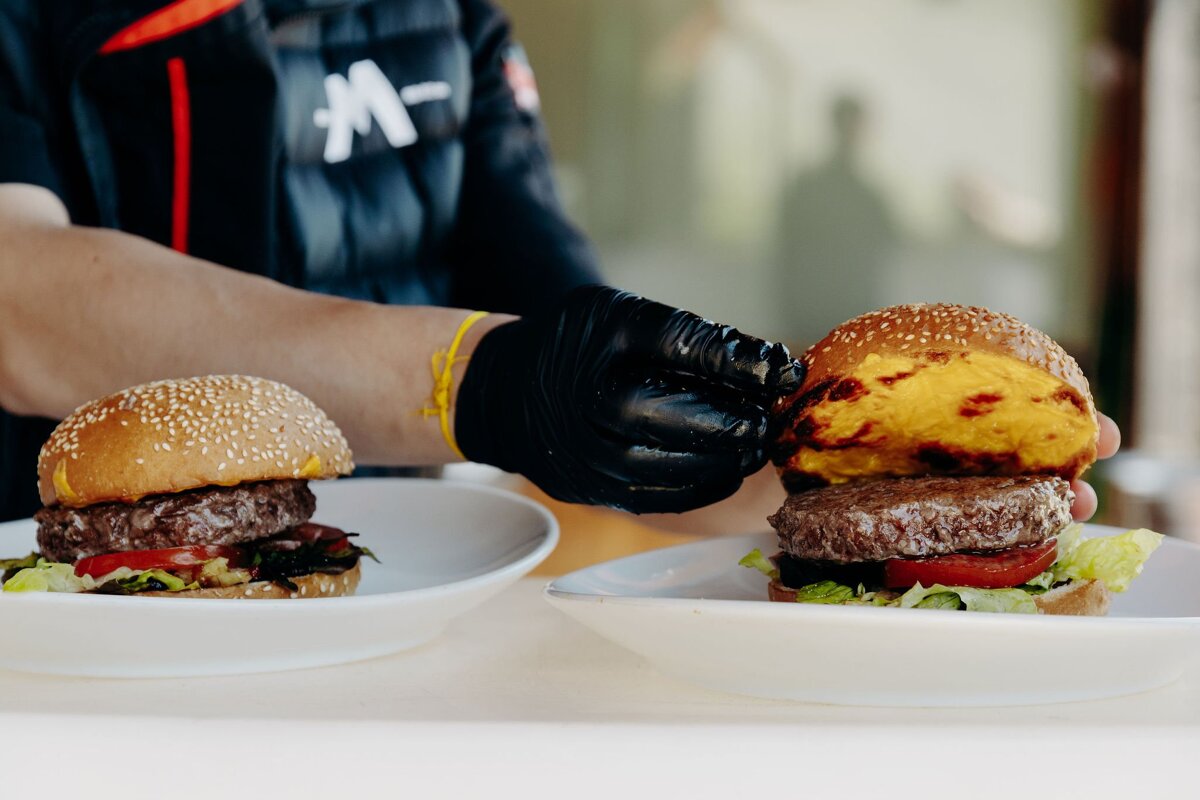A person wearing black gloves is preparing two hamburgers