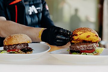 A person wearing black gloves is preparing two hamburgers