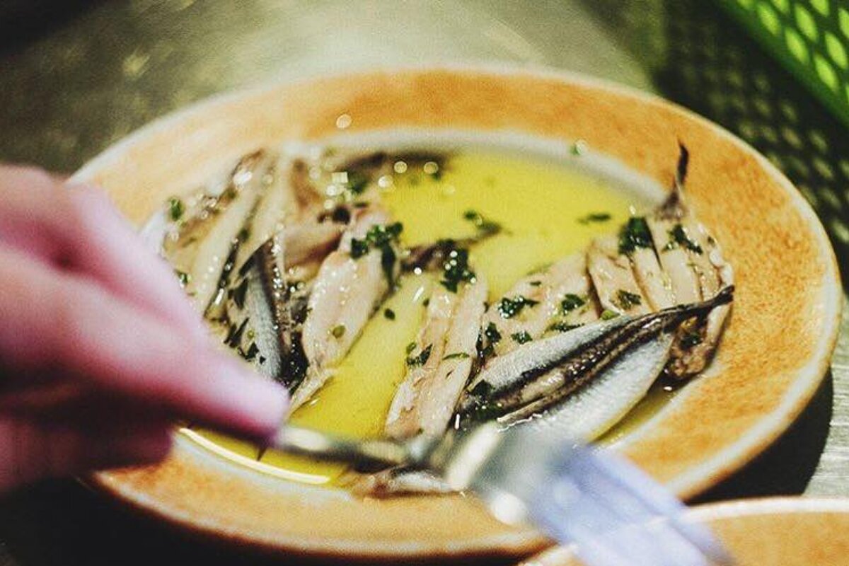 A person is cutting anchovies on a plate with a fork