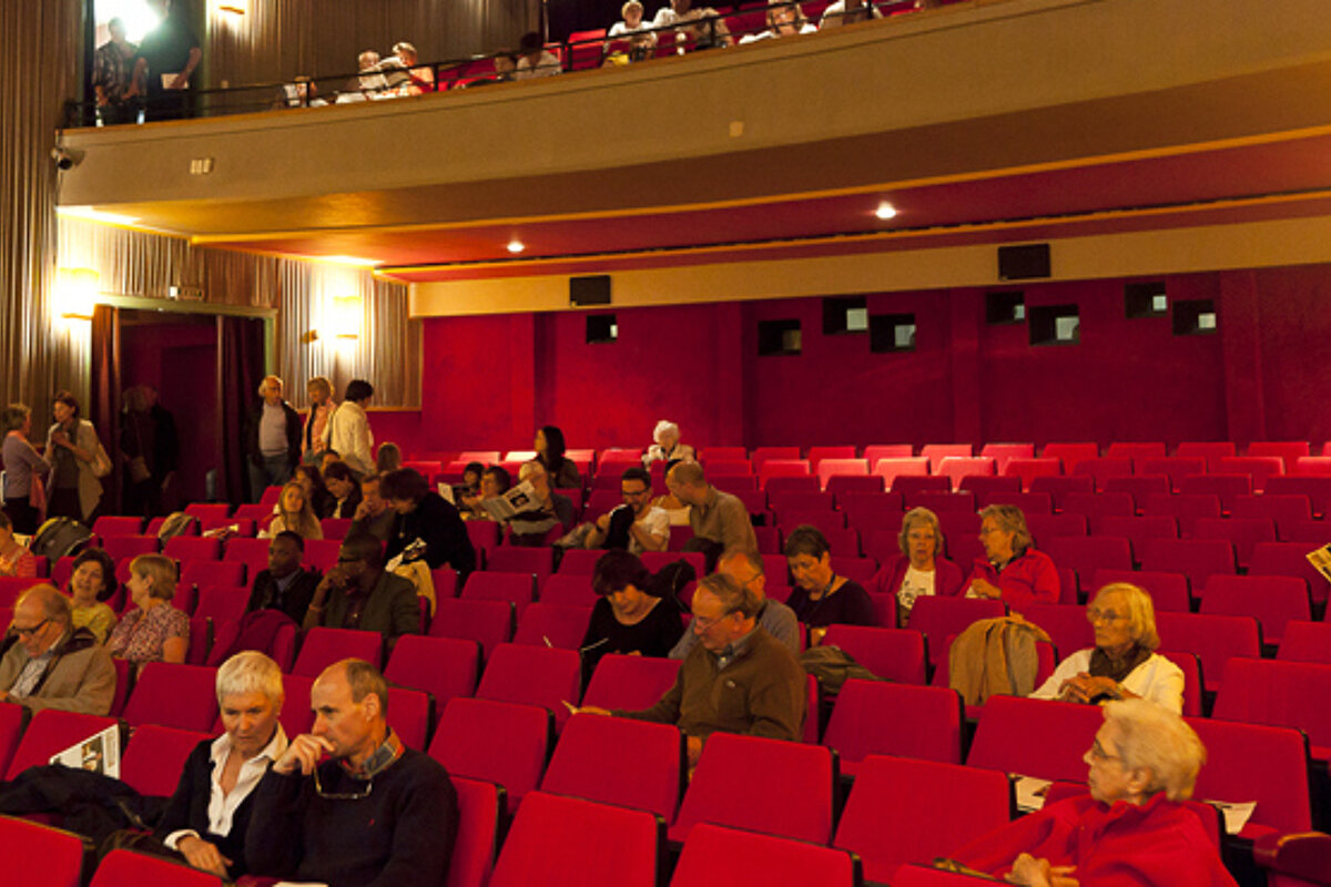 A group of people are sitting in an auditorium with red seats
