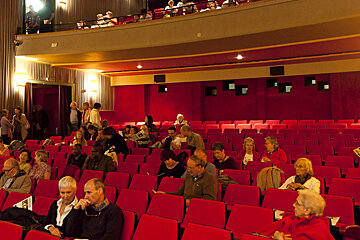 A group of people are sitting in an auditorium with red seats