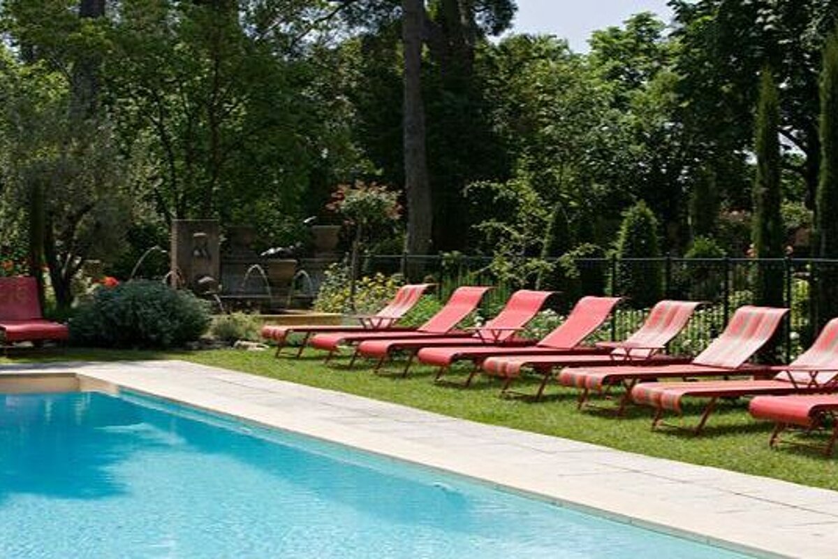 Simple swimming pool with red deck chairs and gardens in the background