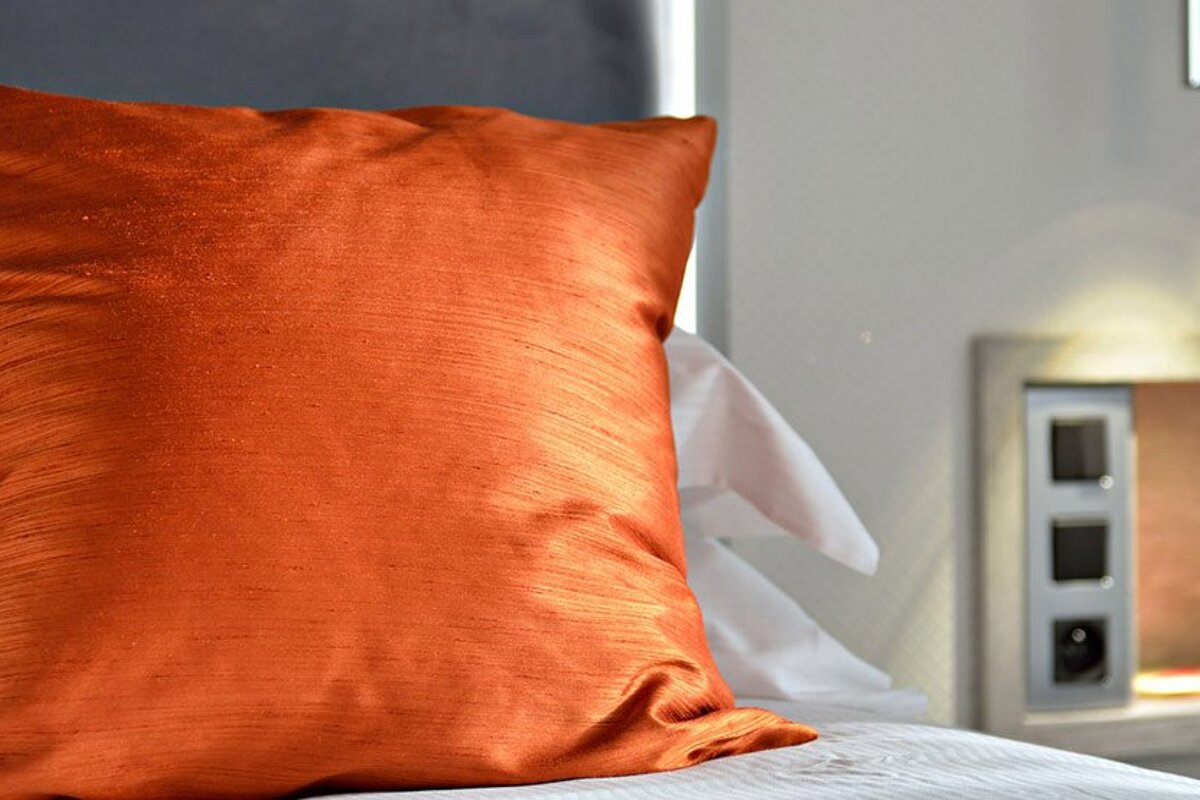 An orange pillow sits on a bed with white sheets