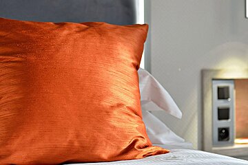 An orange pillow sits on a bed with white sheets