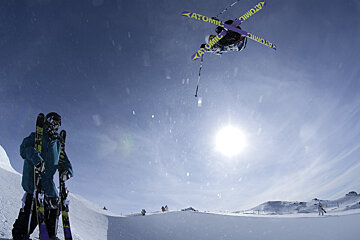 a skier watching another freestyle skier fly through the air
