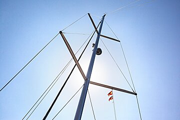 Looking up at a sailboat mast with two flags on it