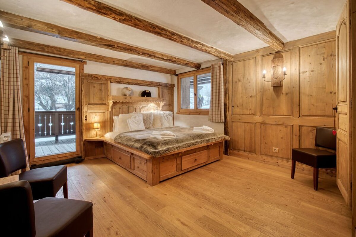 A wooden bedroom with a bed and chairs