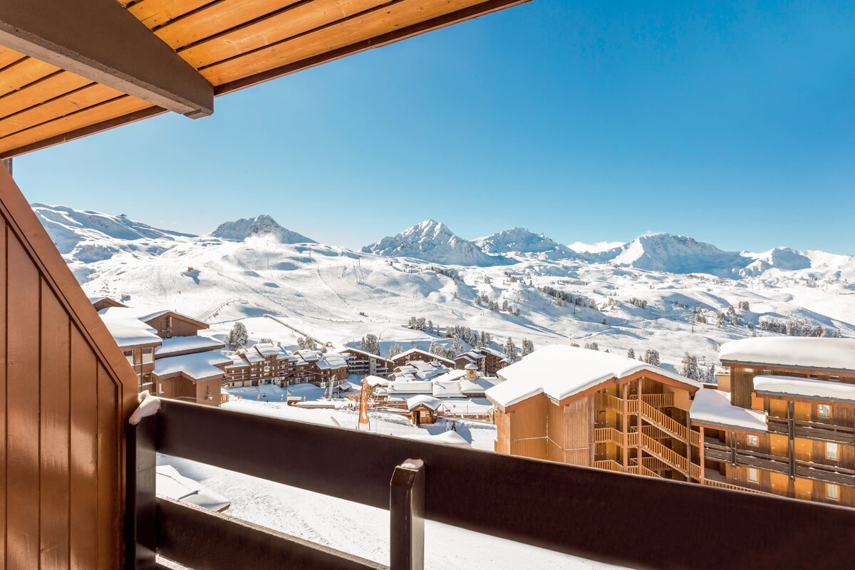 A balcony overlooking a snowy ski resort with mountains in the background