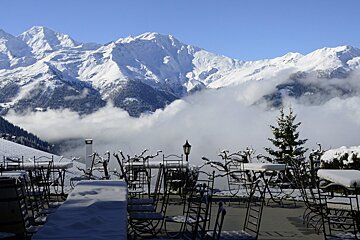 Snow covered tables and chairs with mountains in the background