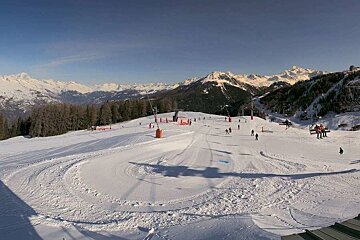 A sunny ski resort with snow-covered slopes, skiers, chairlifts, and majestic snow-capped mountains in the background.