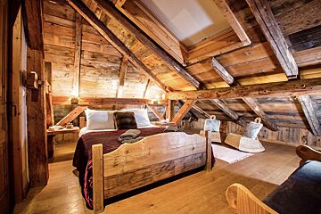 Cozy, rustic attic bedroom built with warm-toned wood, featuring a large bed, exposed beams, and a skylight, creating a charming retreat.