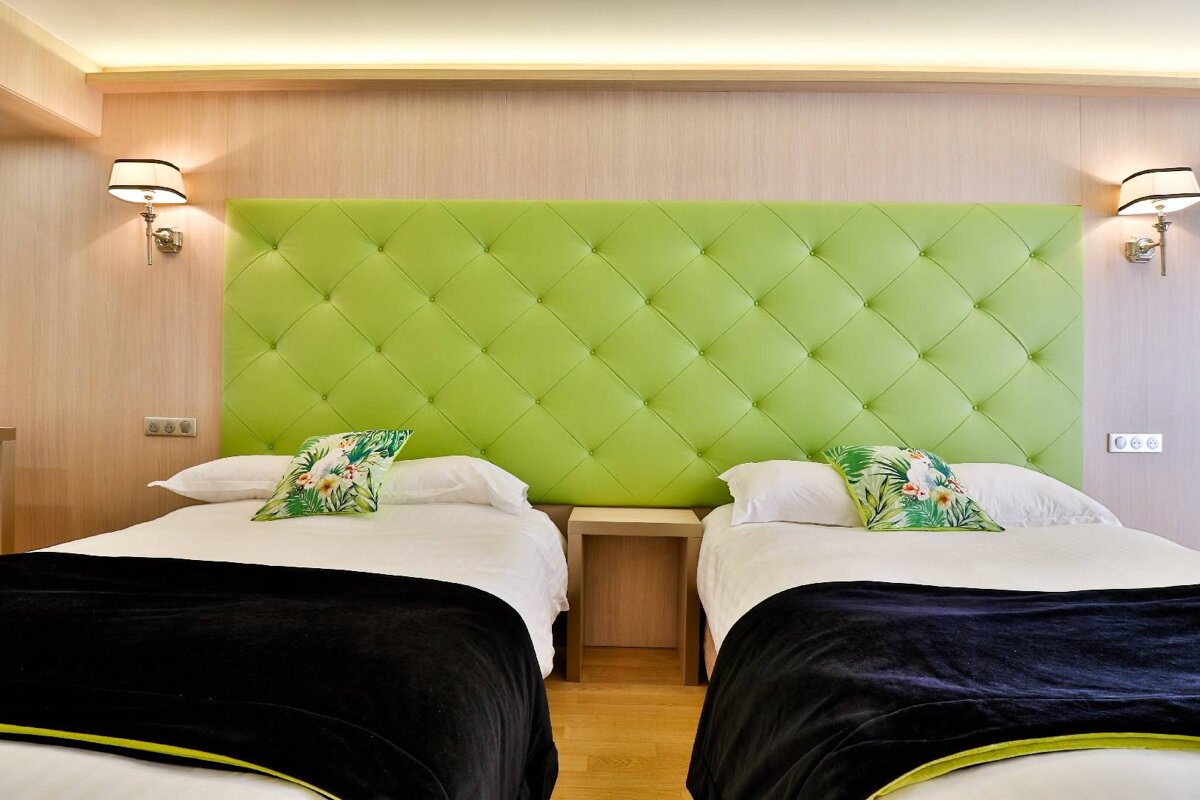 Two beds in a hotel room with a green headboard