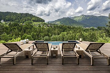 A deck with chairs and a pool with mountains in the background