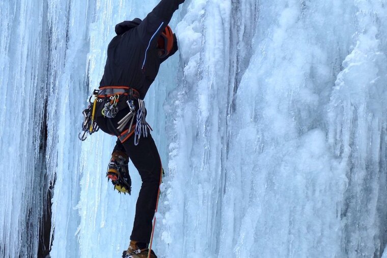 a man scaling a frozen waterfall in climbing gear