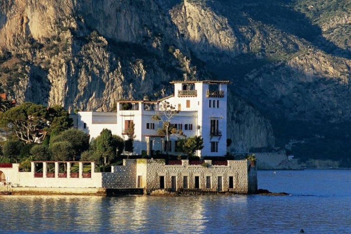 A large white house sits on a small island in the middle of a body of water