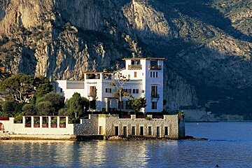 A large white house sits on a small island in the middle of a body of water