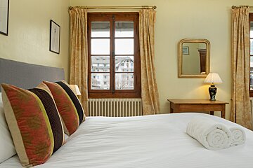 A bedroom with a large window and a table with a lamp on it