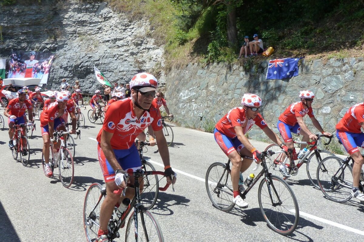 A group of cyclists are riding down a road with flags behind them