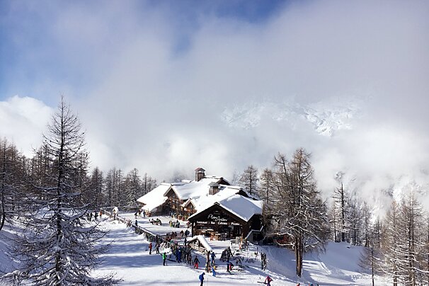 People skiing in front of a snow covered building that says 