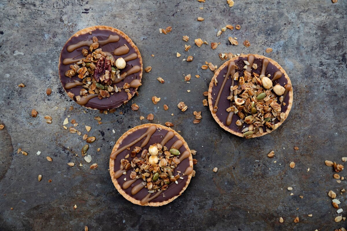 Three cookies with chocolate and granola on them are on a table