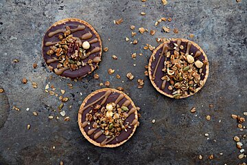 Three cookies with chocolate and granola on them are on a table