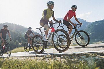A group of cyclists are riding down a road with mountains in the background