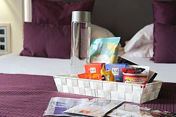 A basket filled with snacks and a bottle of vodka sits on a bed