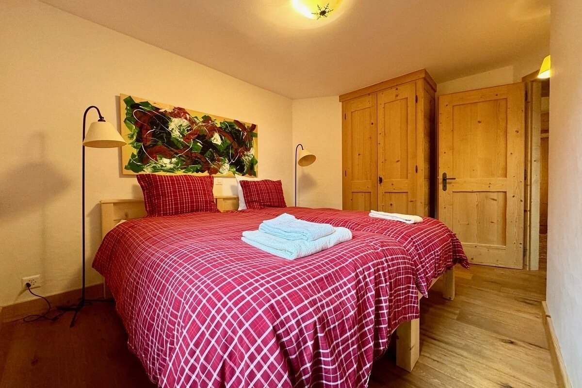Cozy room with twin beds, red plaid bedding, abstract art, light wood furniture, and warm lighting.