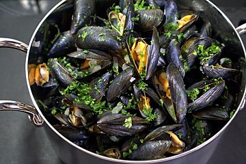 A pot filled with mussels and parsley on a black surface