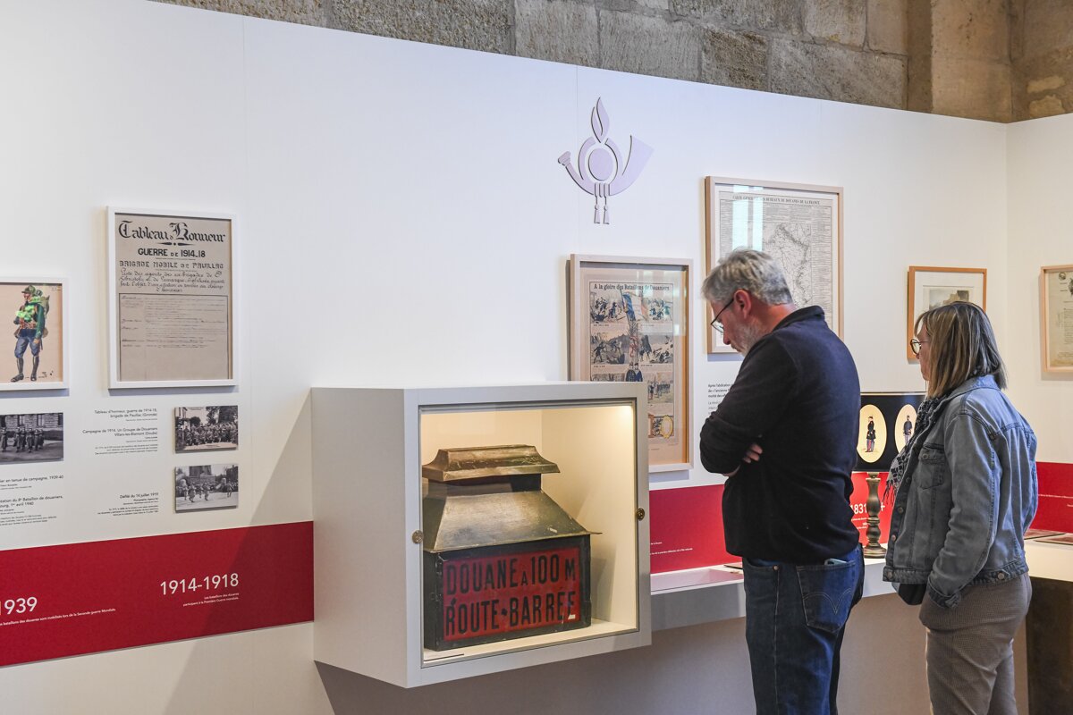 Two people observe various historical exhibits in a brightly lit museum, including framed documents, photos, and an artifact in a display case.