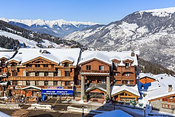 A picturesque snow-covered ski resort village featuring traditional wooden chalets, ski slopes, and majestic snow-capped mountains under a clear blue sky.