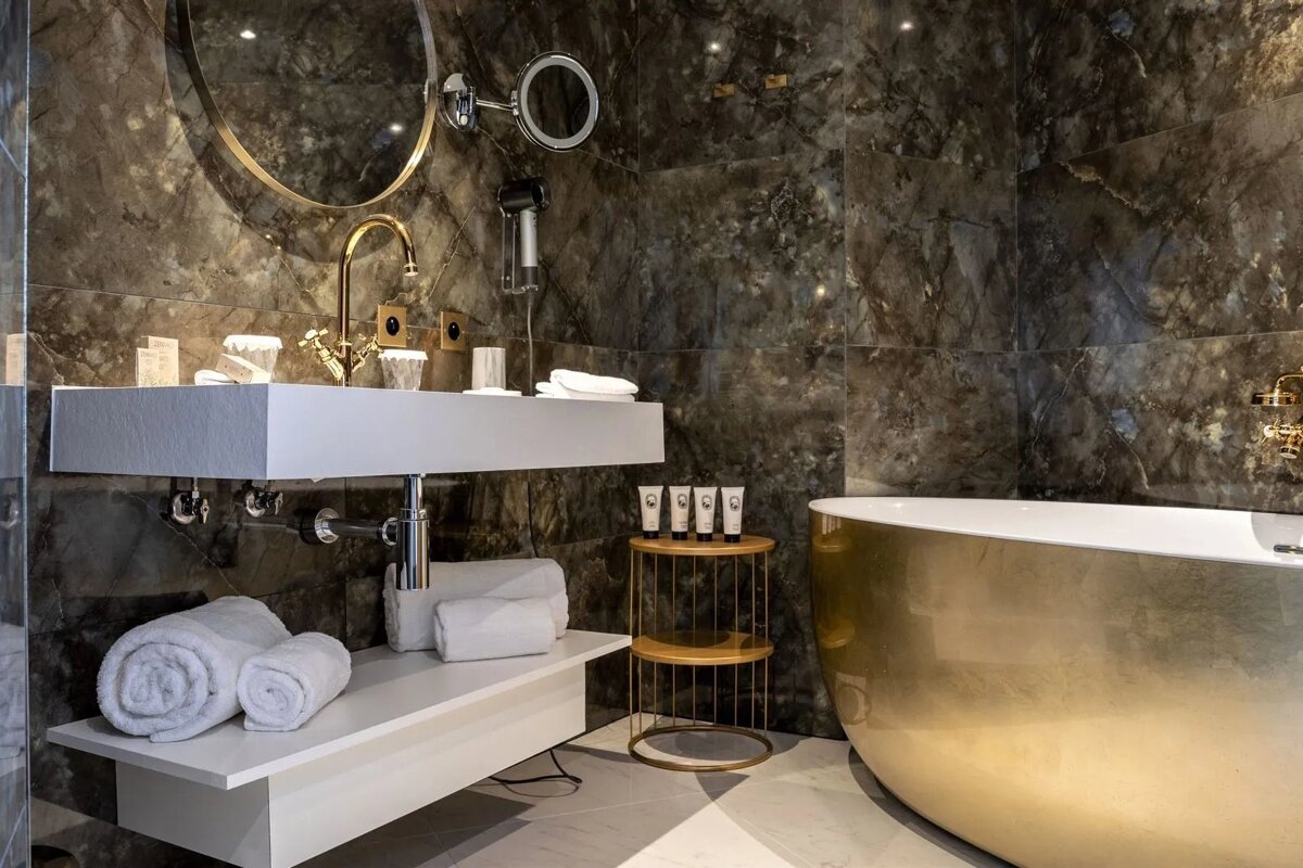 Luxurious modern bathroom featuring dark marble walls, a white floating vanity with a gold faucet, and a striking gold bathtub.