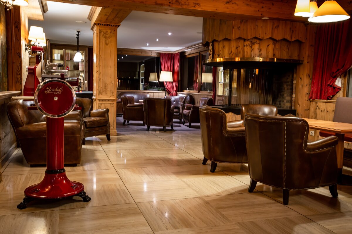 A warmly lit, wood-paneled lounge featuring brown leather armchairs, a large fireplace, and a prominent red Berkel scale on a tiled floor.