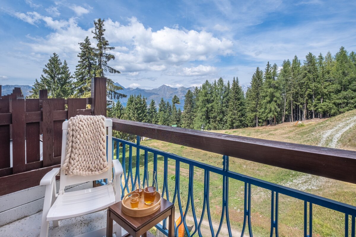 A chair with a blanket on it sits on a balcony overlooking the mountains