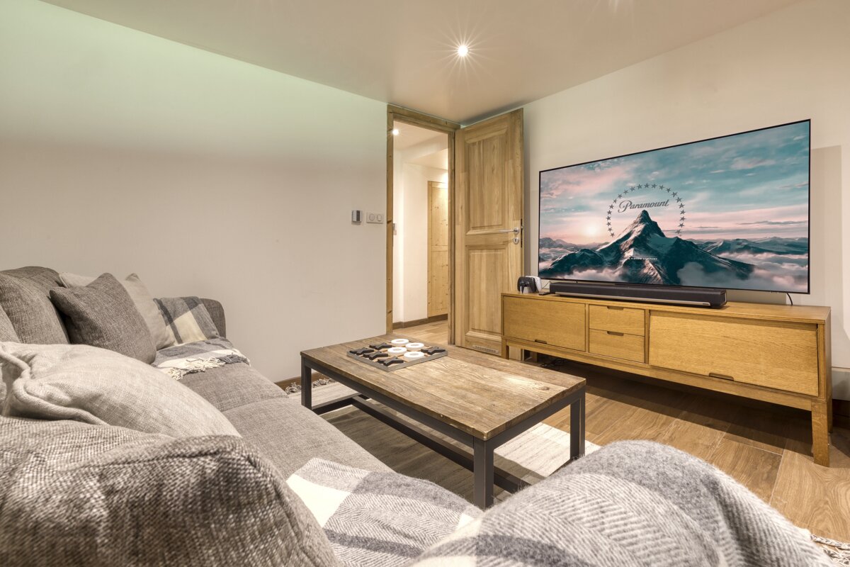 A modern living room with a gray sectional sofa, a wooden coffee table with a game, and a large TV displaying the Paramount logo.