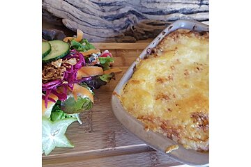 A casserole dish next to a salad on a wooden cutting board