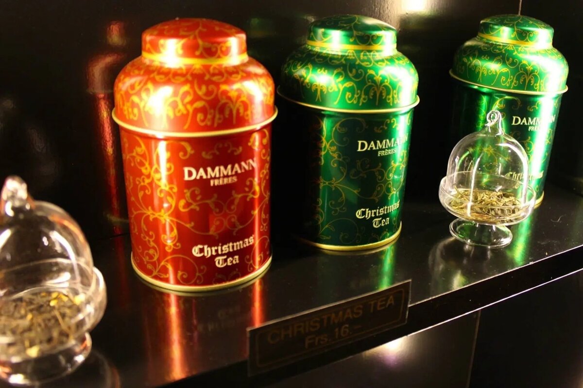 Red & green Dammann Frères Christmas Tea tins are displayed with glass cloches of tea leaves & a