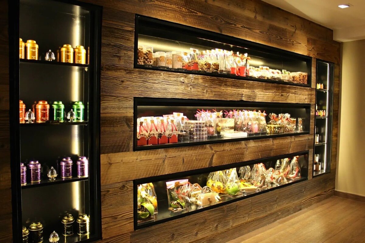 Rustic wooden wall panels with built-in, illuminated display shelves holding colorful tea caddies, packaged sweets, and gifts.