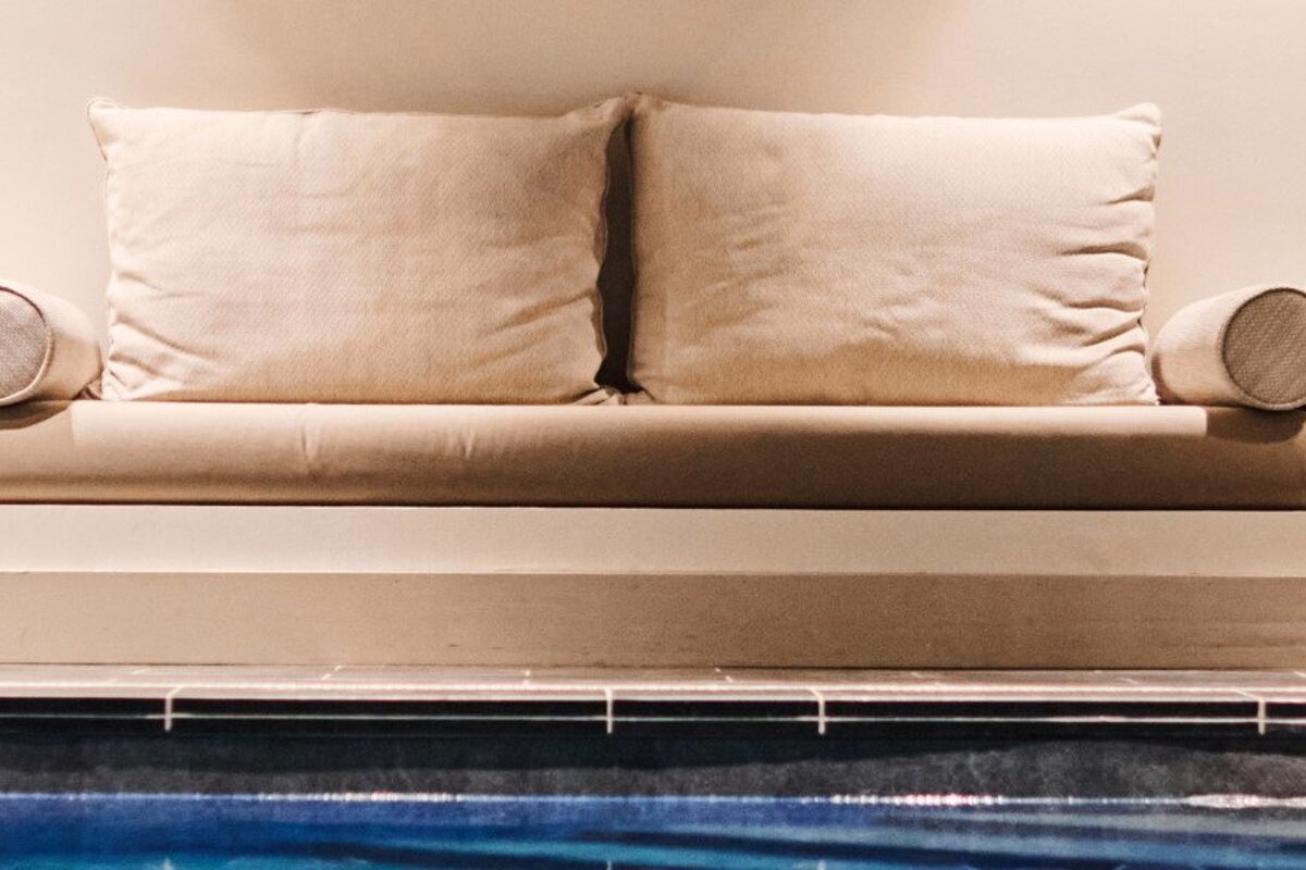 A couch with two pillows sits next to a pool