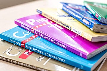 Several books are stacked on top of each other including one called progressive du francais